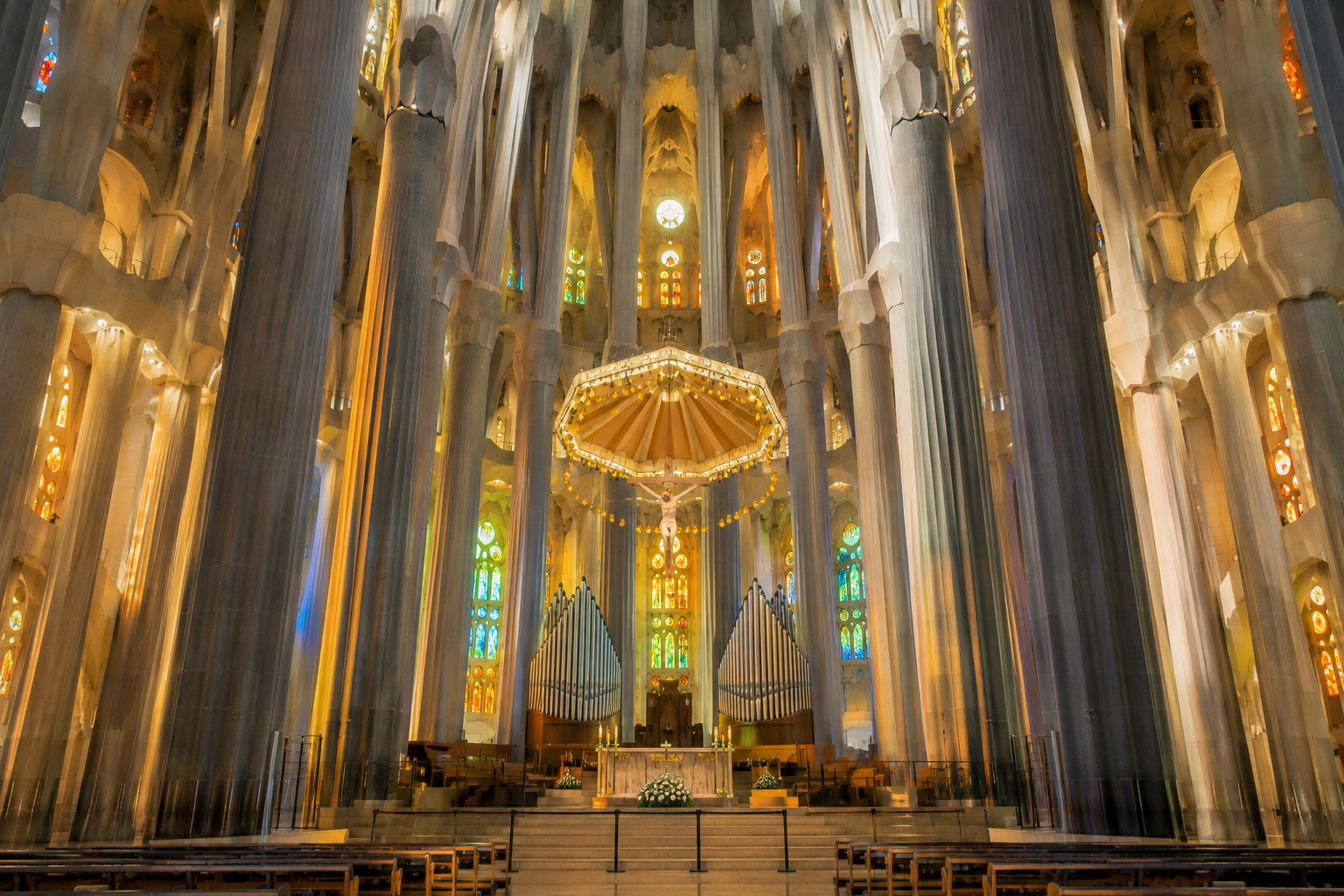 Central altar and apse inside Sagrada Familia in Barcelona beneath the suspended baldachin and crucifix.